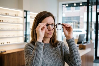 Femme hésitante en train d'examiner des montures de lunettes dans une boutique d'optique moderne